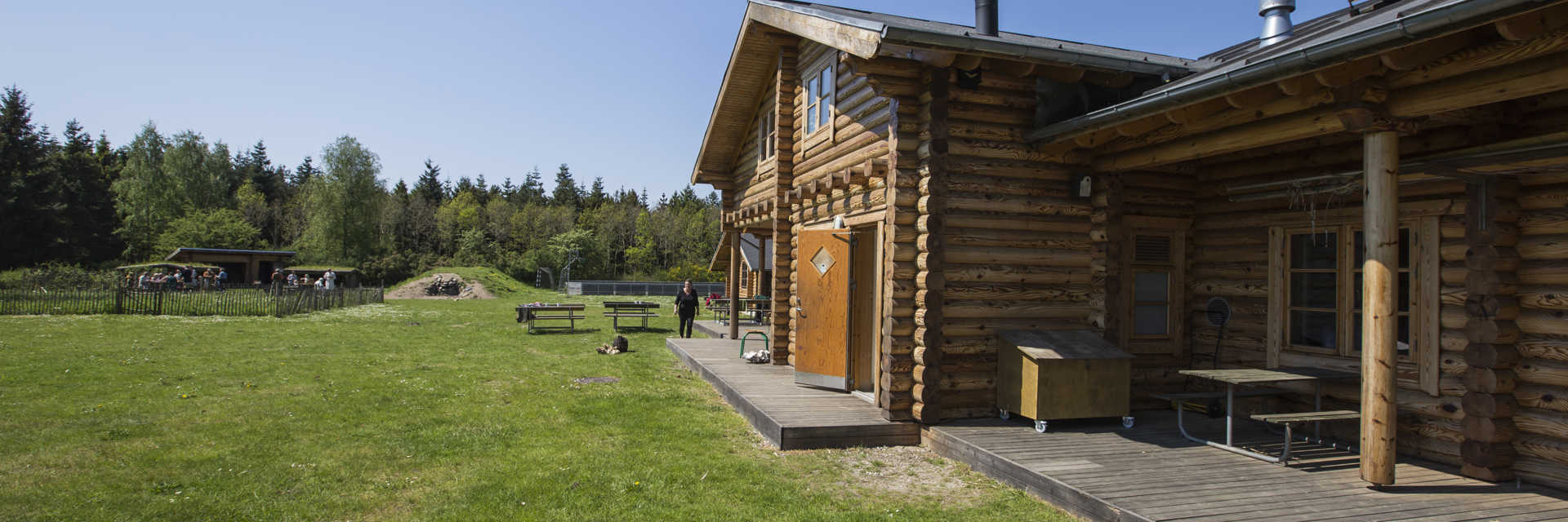 Bjælkehytte på grøn græsplæne og træer i baggrunden