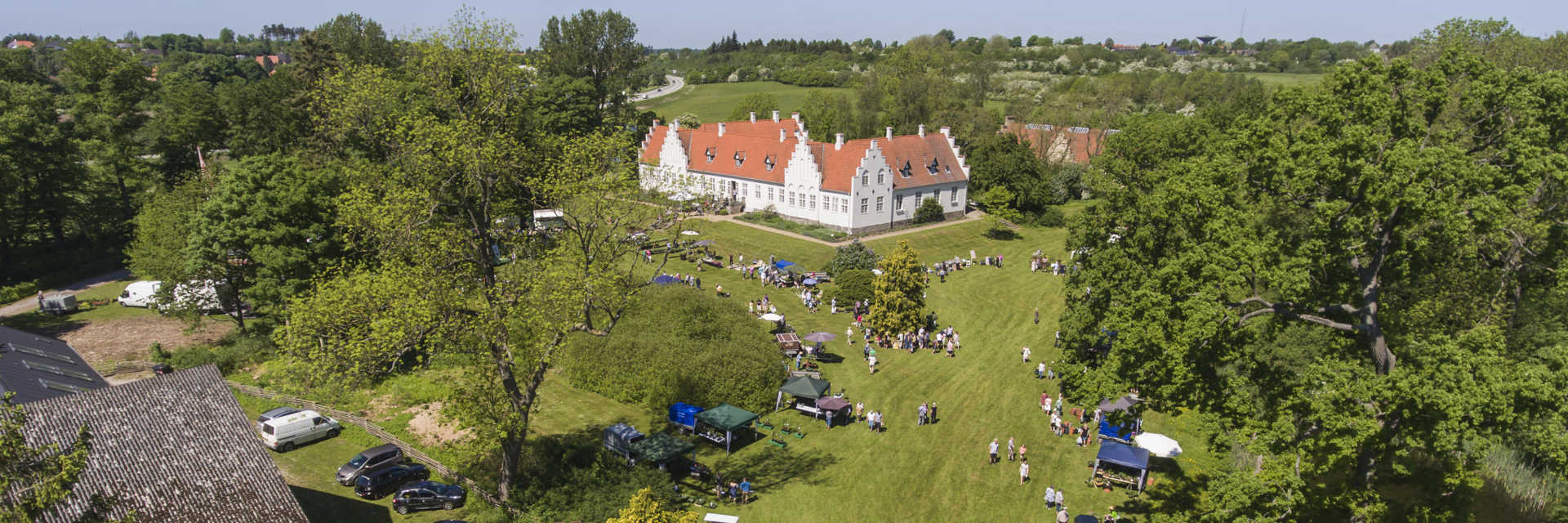 Hvid bygning på græsplæne med omkringliggende træer en sommerdag